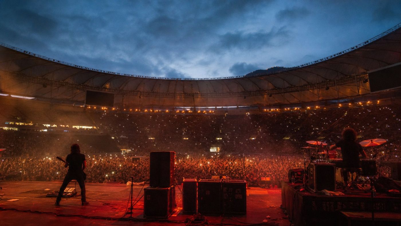 Palco de rock visto diante de estádio lotado ao anoitecer. Imagem ilustrativa gerada por IA para o ClickFato.